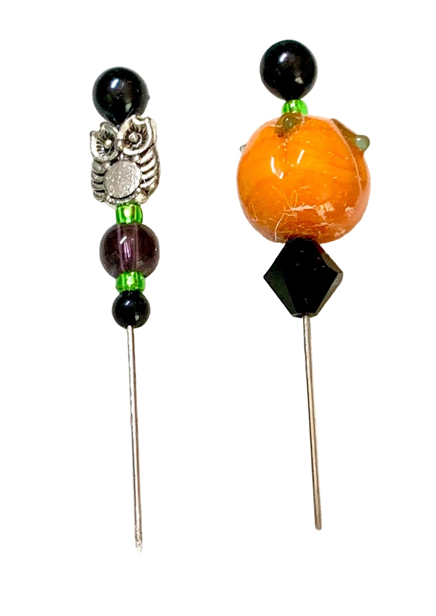 Two beaded pins, featuring black beads, a silver owl charm, green spacer beads, a purple bead, and a large orange pumpkin bead on the right.
[additional_image_link]
