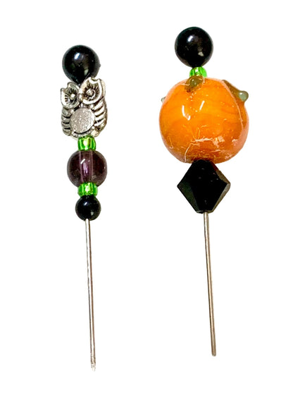 Two beaded pins, featuring black beads, a silver owl charm, green spacer beads, a purple bead, and a large orange pumpkin bead on the right.
[additional_image_link]