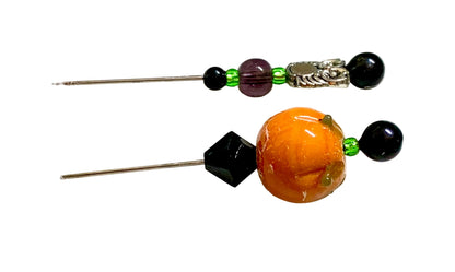 Two handmade pins, featuring a large orange pumpkin bead, a black faceted bead, a black round bead, a purple glass bead, a green spacer bead, and a silver owl charm, displayed on a white surface.
[additional_image_link]