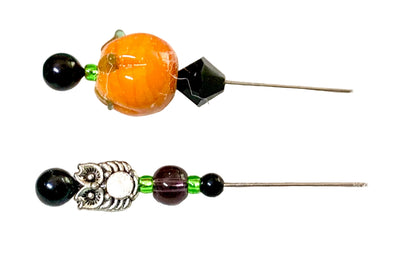 Two beaded pins displayed horizontally on a plain white background. The top pin features a large orange glass bead, a small green bead, a black faceted bead, and a silver owl pin.
[additional_image_link]