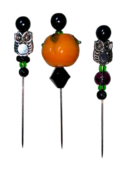 Three decorative  Halloween pins with 1 pumpkin, 2 owls, several green, purple and black glass beads designs on a white background.
[additional_image_link]