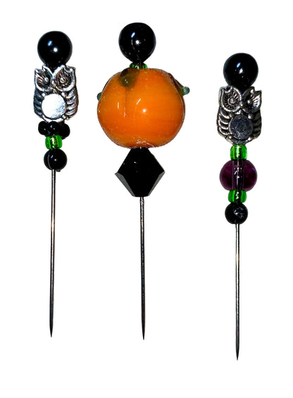 Three decorative  Halloween pins with 1 pumpkin, 2 owls, several green, purple and black glass beads designs on a white background.
[additional_image_link]