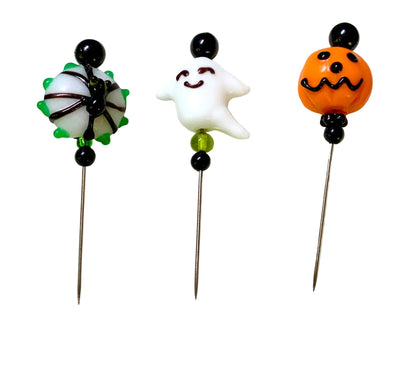 Three Halloween-themed glass bead pins on metal needles, featuring a spider, a smiling ghost, and a jack-o'-lantern, displayed on a white background.
[additional_image_link]