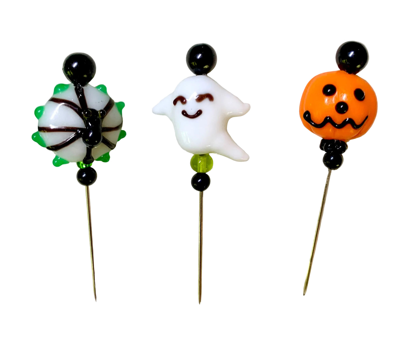 Three Halloween-themed glass pins on a white background. The left pin features a white spider with green accents and black details. The middle pin is a smiling ghost. The right pin is a jack-o'-lantern.
[additional_image_link]