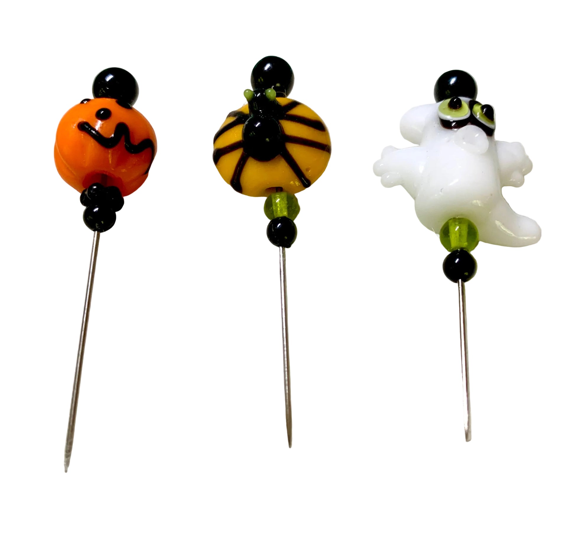 Three Halloween-themed glass bead pins on metal needles, featuring an orange jack-o'-lantern, a spider on a yellow bead, and a white ghost, displayed on a white surface.
[additional_image_link]