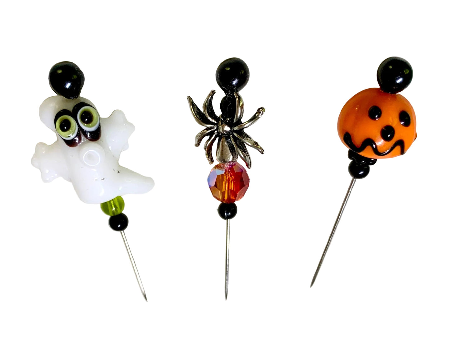Three Halloween-themed beaded sewing pins displayed on a white surface. The right needle has an orange jack-o'-lantern bead with black details, the middle bead has a silver spider bead with a faceted orange crystal, and the left needle has a white ghost bead with green eyes.
[additional_image_link]