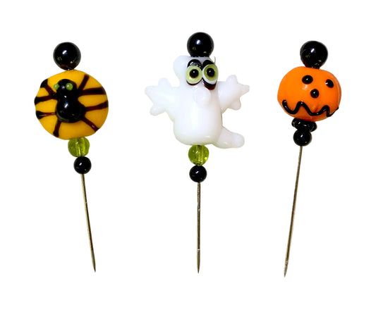 Three Halloween-themed glass beaded pins on a white background. One pin features a spider on a yellow bead, one pin features a white ghost, and one pin features an orange jack-o'-lantern.
[image_link]
