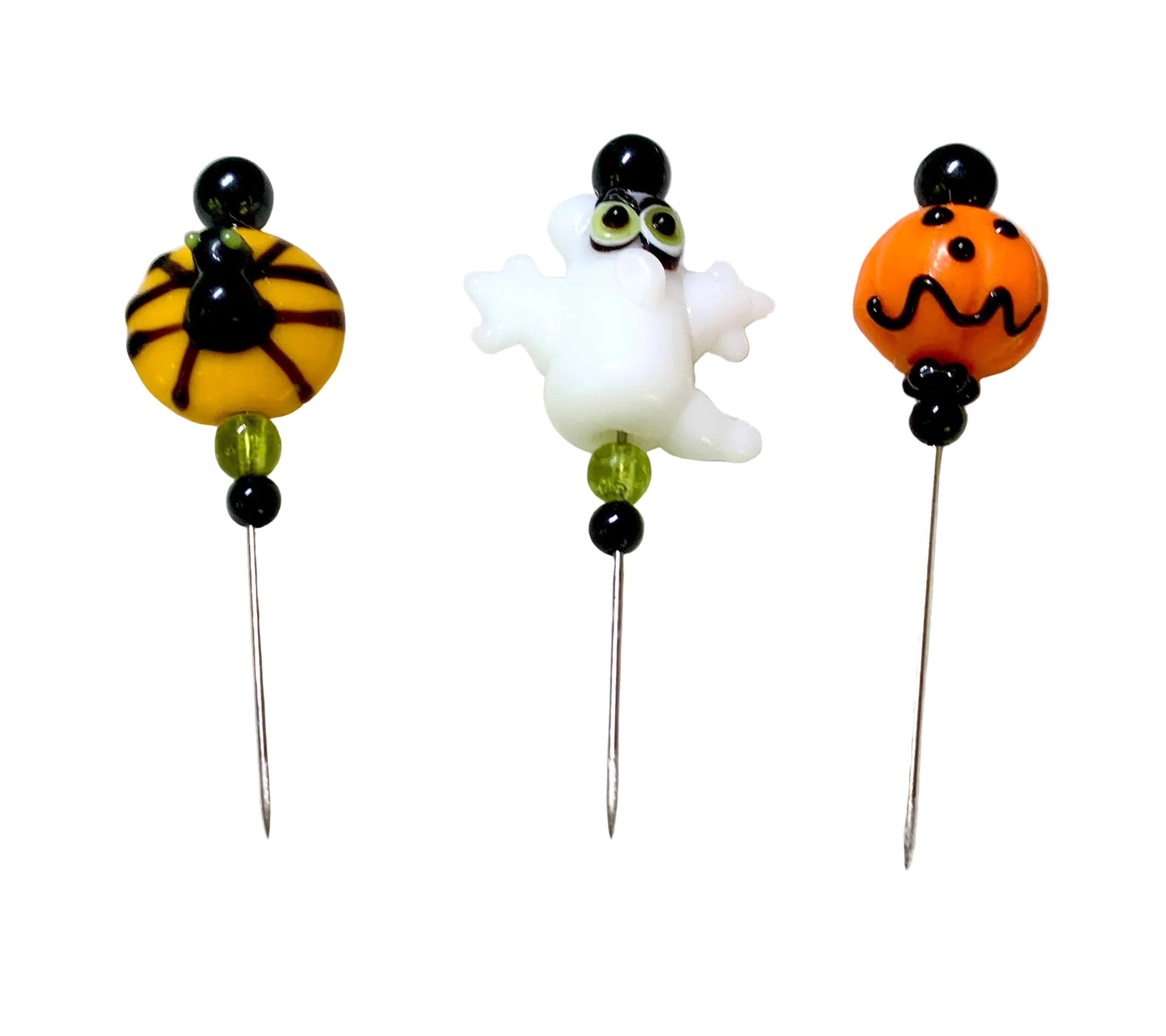 Three Halloween-themed glass beaded pins on a white background. One pin features a spider on a yellow bead, one pin features a white ghost, and one pin features an orange jack-o'-lantern.
[additional_image_link]