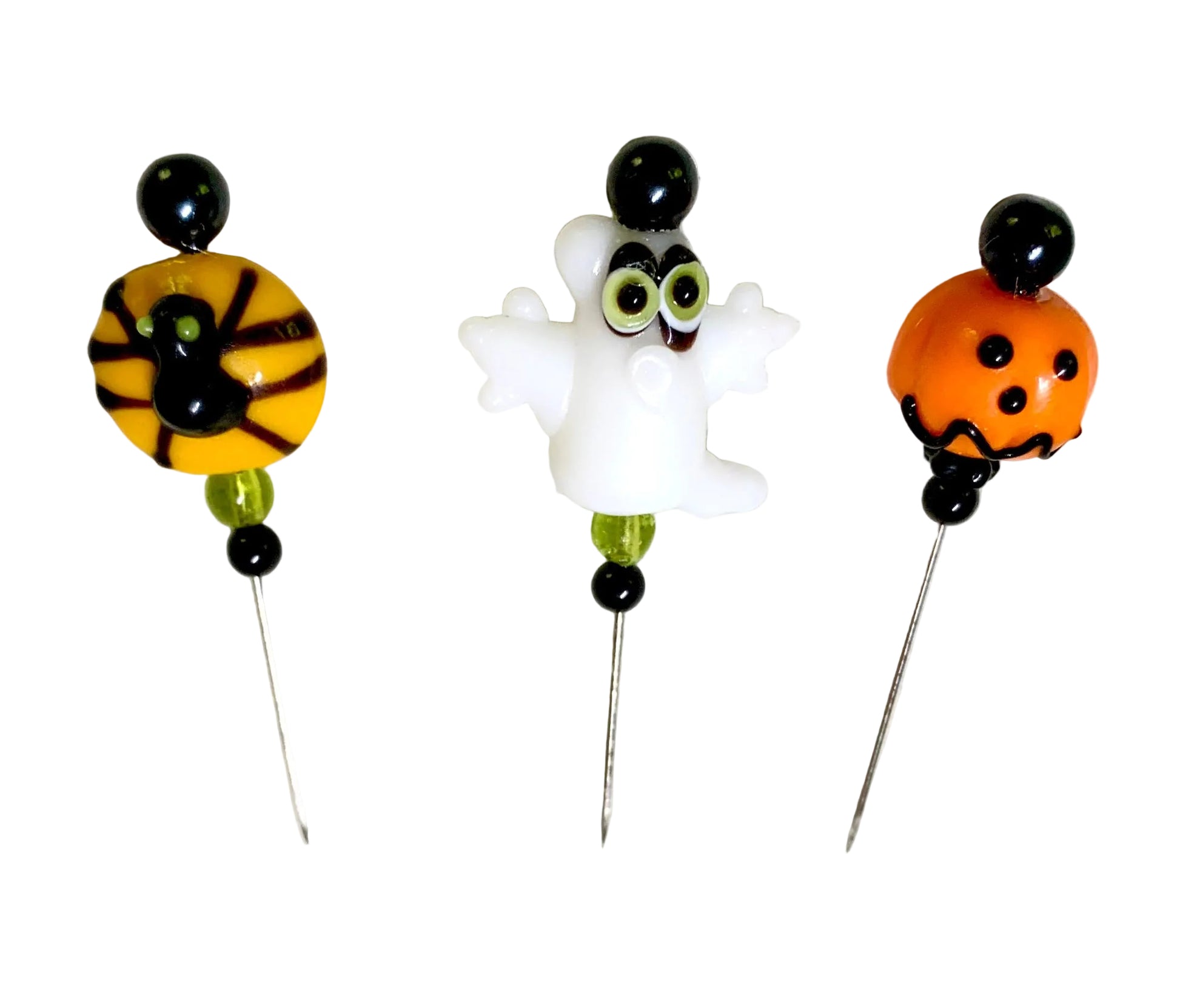 Three Halloween-themed glass beaded pins on a white background. One pin features a spider on a yellow bead, one pin features a white ghost, and one pin features an orange jack-o'-lantern.
[additional_image_link]