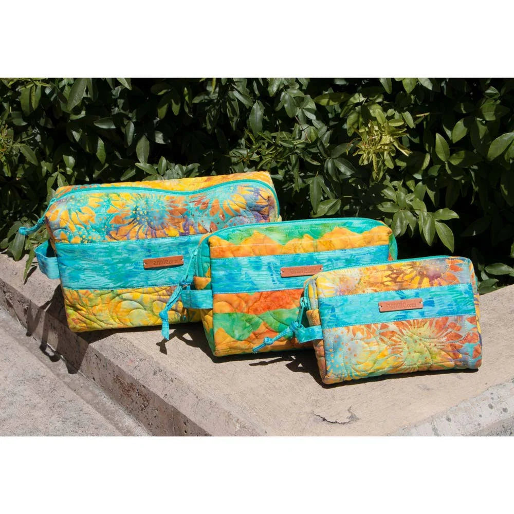 Three colorful zippered pouches in different sizes with a vibrant tie-dye floral pattern, displayed on a stone ledge with green foliage in the background.
Photo by Annie [additional_image_link]