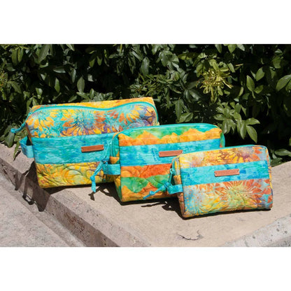 Three colorful zippered pouches in different sizes with a vibrant tie-dye floral pattern, displayed on a stone ledge with green foliage in the background.
Photo by Annie [additional_image_link]