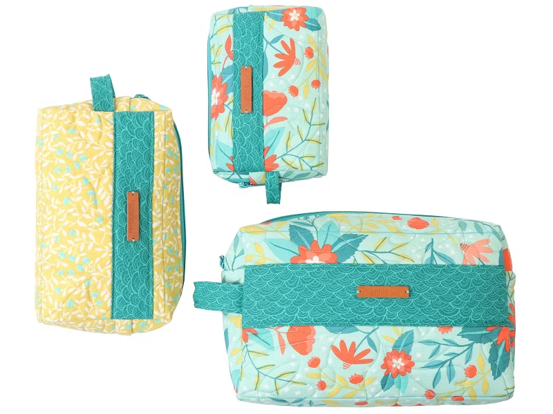 Three fabric pouches or bags shown on a plain white background: one tall yellow-and-teal patterned bag, one smaller matching teal-and-white floral bag, and one larger teal-and-white floral bag with a wide teal strap and tan logo patch.
Photo by Annie [additional_image_link]