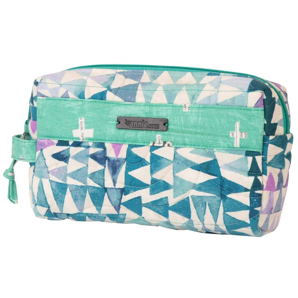 A rectangular zippered pouch with a geometric triangle pattern in teal, blue, purple, and white, featuring a turquoise front pocket and a metal brand plate reading 'by annie.com'.
Photo by Annie [additional_image_link]