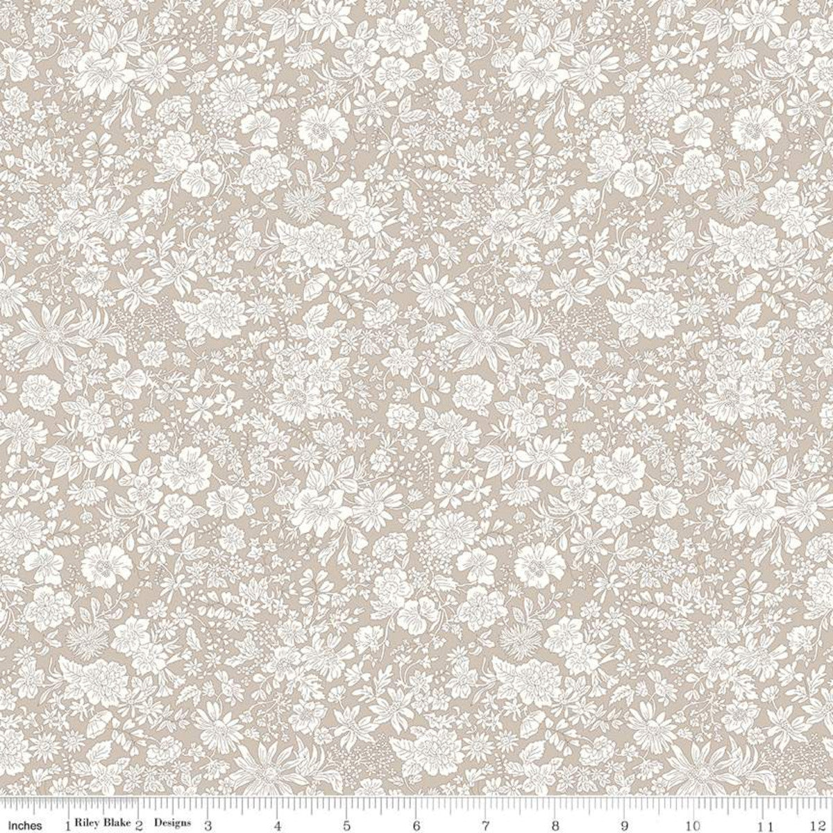 A close-up of a fabric pattern featuring a delicate white floral and leaf print on a warm beige background, with a ruler at the bottom indicating scale.