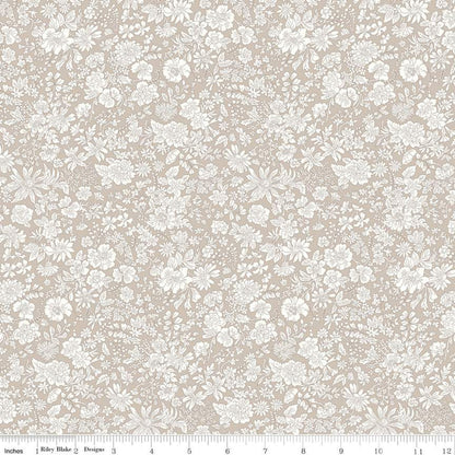 A close-up of a fabric pattern featuring a delicate white floral and leaf print on a warm beige background, with a ruler at the bottom indicating scale.