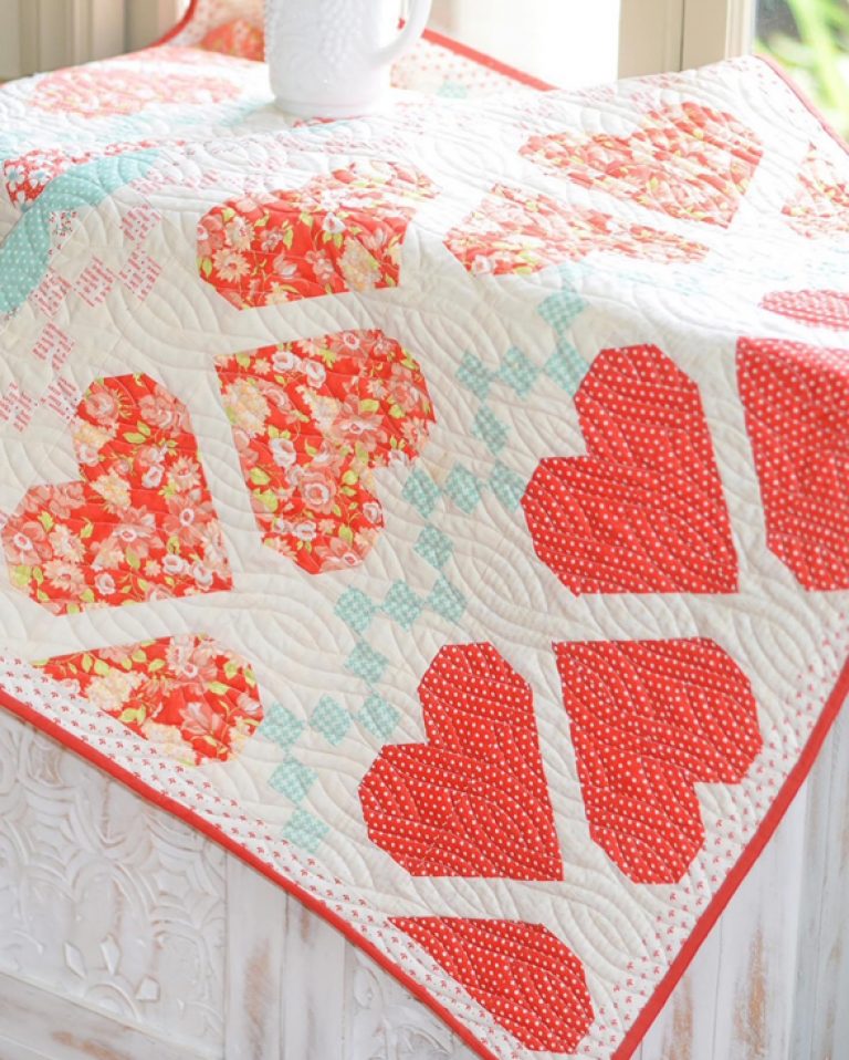 A quilt 'Fair Isle Hearts' by Joanna Figueroa, showing a quilt with red and white heart shapes on a white background, and a detail of a quilt block with various red prints.
Photo by Fig Tree & Co. [additional_image_link]