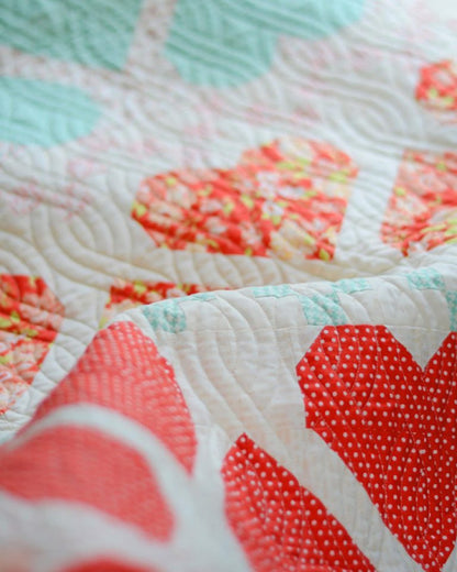 A quilt 'Fair Isle Hearts' by Joanna Figueroa, showing a quilt with red and white heart shapes on a white background, and a detail of a quilt block with various red prints.
Photo by Fig Tree & Co. [additional_image_link]