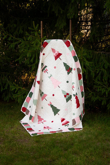 A quilted blanket with a Christmas tree pattern, draped over a wooden stand outdoors on a grassy lawn with dark green trees in the background.
Photo by My Sew Quilty Life [additional_image_link]