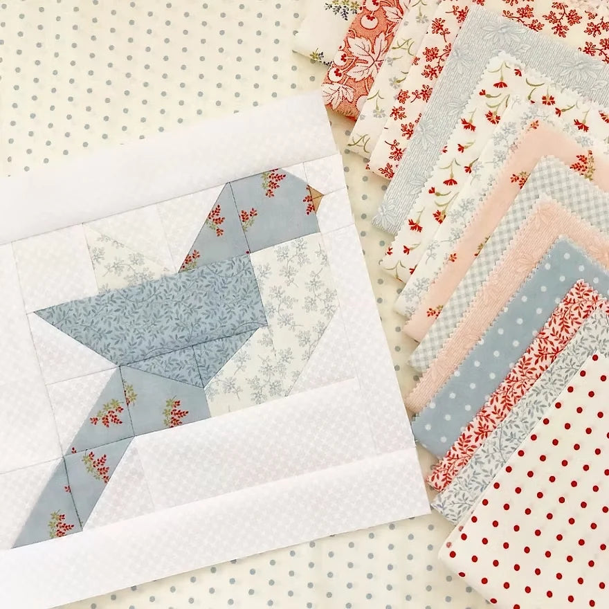 A quilted bird patchwork piece made from light blue, white, and floral fabrics, displayed next to a stack of matching patterned fabric swatches on a polka-dot background.
Photo by ThePatternBasket.com [additional_image_link]