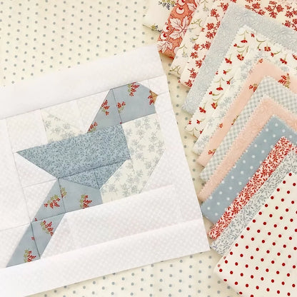 A quilted bird patchwork piece made from light blue, white, and floral fabrics, displayed next to a stack of matching patterned fabric swatches on a polka-dot background.
Photo by ThePatternBasket.com [additional_image_link]