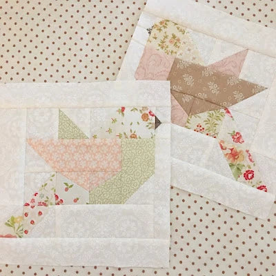 Two quilted bird block pieces arranged on a beige polka dot fabric background. The blocks feature a bird made from pink, sage green, and floral patterned fabric patches.
Photo by ThePatternBasket.com [additional_image_link]
