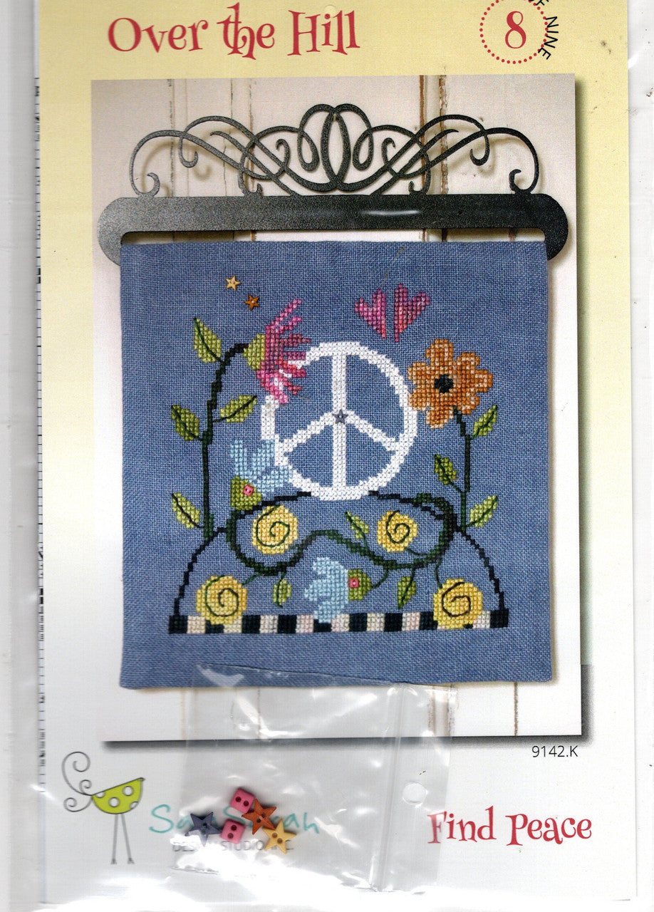 Cross-stitch pattern card for 'Over the Hill' featuring a blue fabric swatch with a peace sign, flowers, and leaves, with small beads and a metal hanger included in the package.
Photo by SamSarah Studio Designs [image_link]