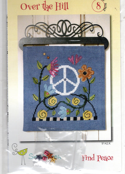Cross-stitch pattern card for 'Over the Hill' featuring a blue fabric swatch with a peace sign, flowers, and leaves, with small beads and a metal hanger included in the package.
Photo by SamSarah Studio Designs [image_link]