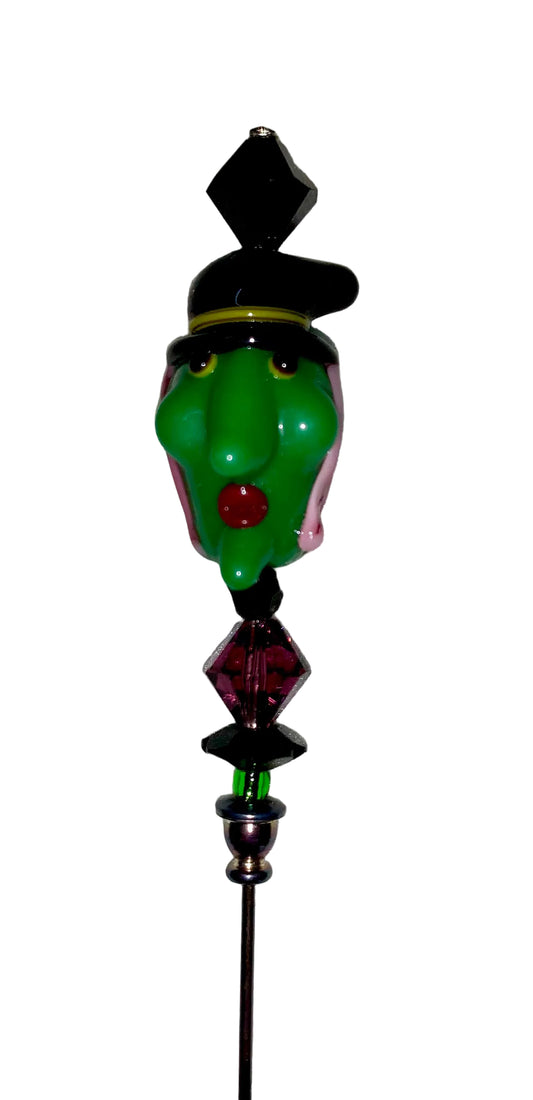 Green witch head with black hat , red lips and pink hair, purple and green and black beads on a 5" hat pin.
[image_link]
