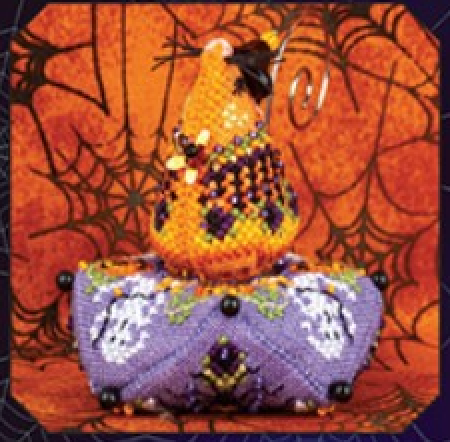 A handmade beaded and crocheted witch hat and matching base decoration, featuring a yellow-orange hat with purple and black details, set against an orange spiderweb background.
Photo by JustNan.com [additional_image_link]