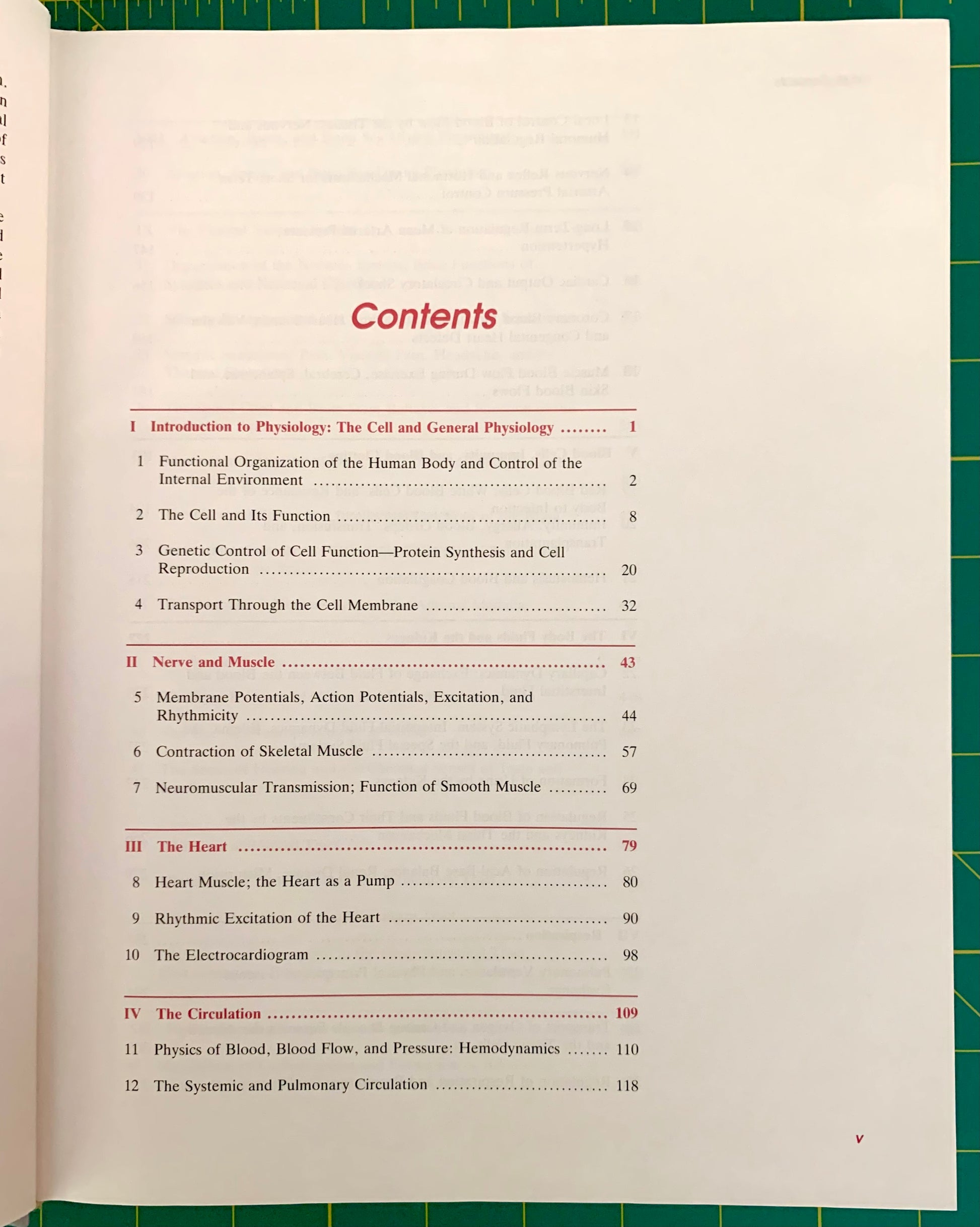An open book page showing the table of contents in red text on an off-white page, photographed on a green cutting mat.
[additional_image_link]
