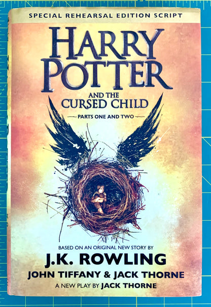 A book cover for 'Harry Potter and the Cursed Child: Parts One and Two' shown flat against a blue grid background. The cover features a warm beige and yellow gradient background with dark blue title text and an illustration of a bird's wings surrounding a nest with a small figure inside.