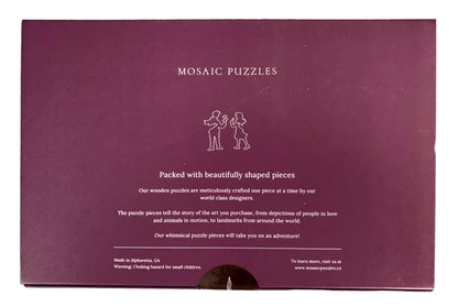 The back of a purple Mosaic Puzzles gift box, showing product description text and a small line drawing of two children assembling a puzzle, placed on a green cutting mat.
Photo by Karen King [additional_image_link]