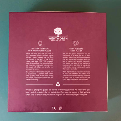 The back of a Wentworth Wooden Puzzles box, featuring product information, a tree logo, and recycling symbols on a dark red background, photographed against a green surface.
Photo by Karen King [additional_image_link]