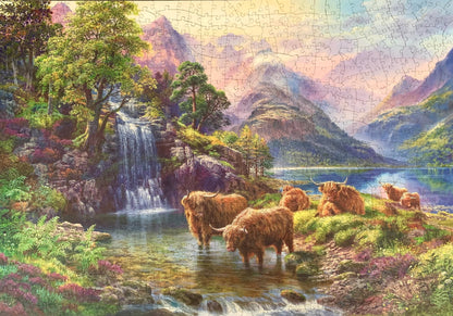 A wooden jigsaw puzzle depicting a highland landscape scene with cows, a waterfall, and mountains in the background.
Photo by Karen King [additional_image_link]