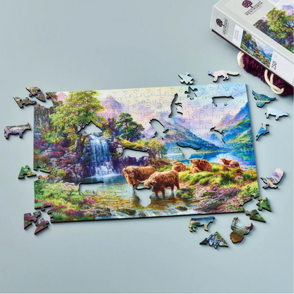 A wooden jigsaw puzzle depicting a highland landscape scene with cows, a waterfall, and mountains in the background.
Photo by Wentworth Puzzles [additional_image_link]