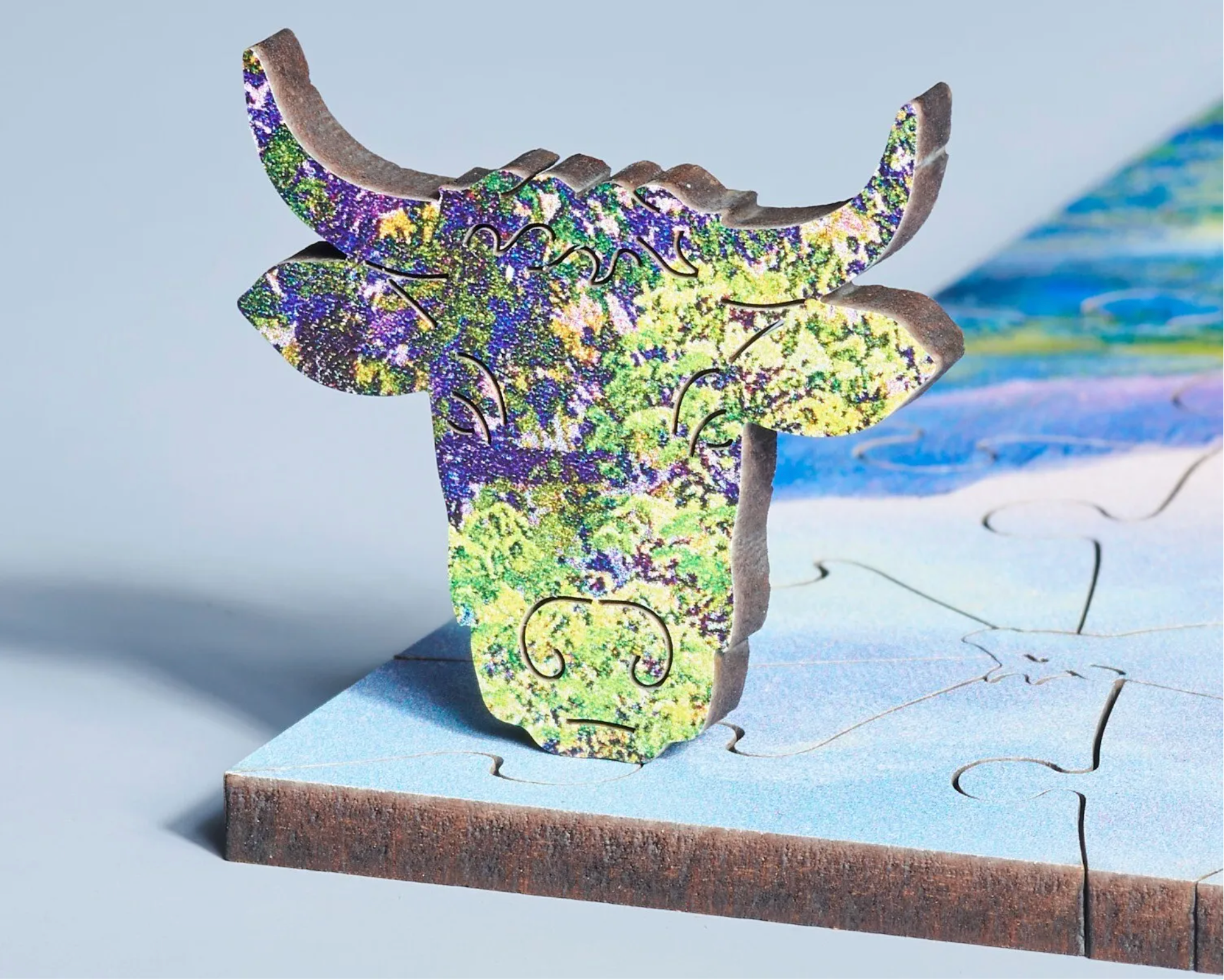 A wooden jigsaw puzzle depicting a highland landscape scene with cows, a waterfall, and mountains in the background.
Photo by Wentworth Puzzles [additional_image_link]