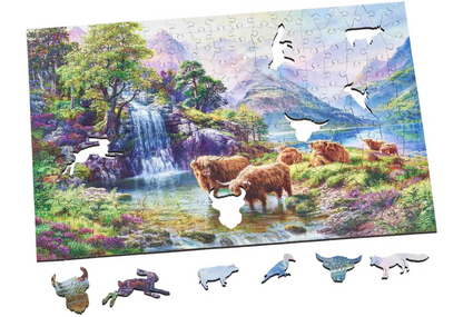 A wooden jigsaw puzzle depicting a highland landscape scene with cows, a waterfall, and mountains in the background.
Photo by Wentworth Puzzles [additional_image_link]