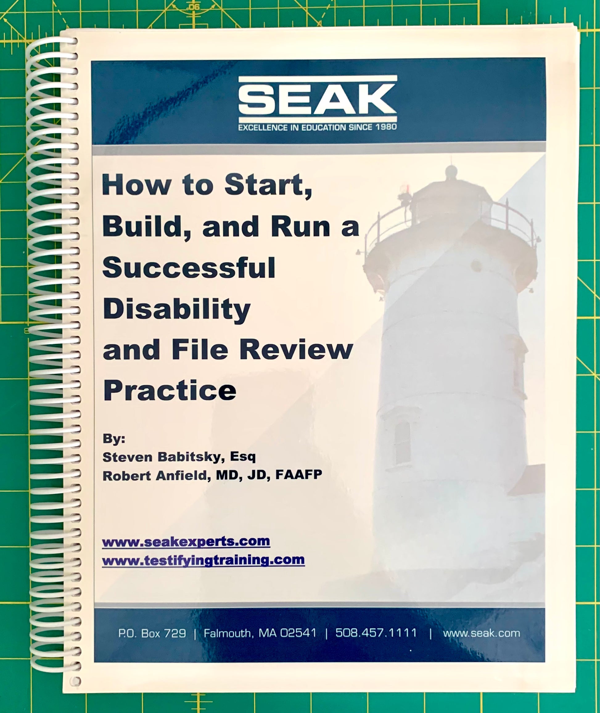 A spiral-bound booklet cover titled 'How to Start, Build, and Run a Successful Disability and File Review Practice' by Steven Babitsky, Esq and Robert Anfield, MD, FAAFP, featuring a lighthouse photo and SEAK branding, placed on a green cutting mat.
[image_link]