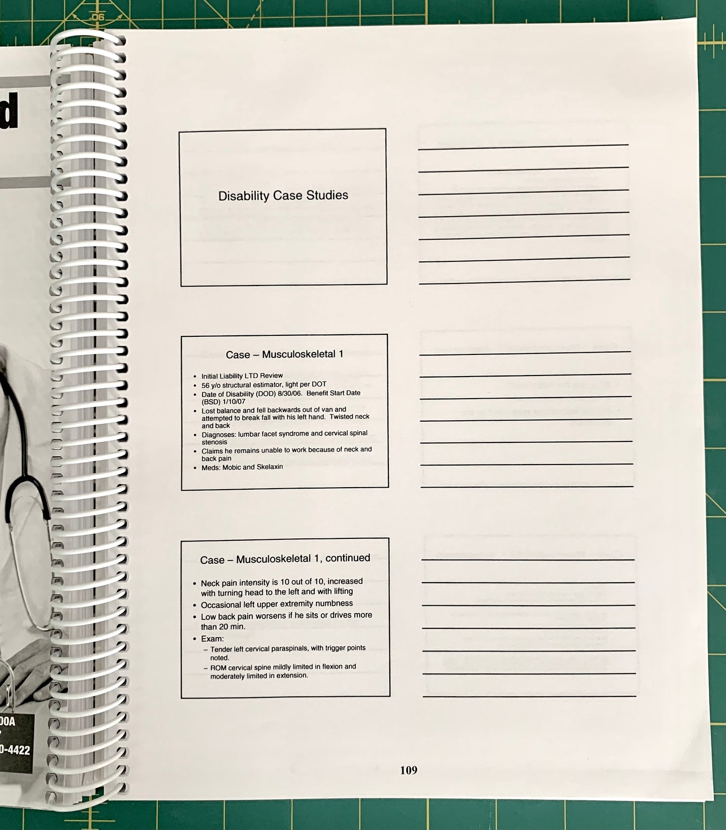 A spiral-bound notebook page titled 'Disability Case Studies' with lined writing space and printed case study text, photographed on a green cutting mat with part of a person's hand and arm visible at the left edge.
[additional_image_link]