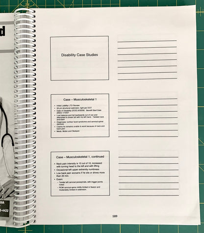 A spiral-bound notebook page titled 'Disability Case Studies' with lined writing space and printed case study text, photographed on a green cutting mat with part of a person's hand and arm visible at the left edge.
[additional_image_link]