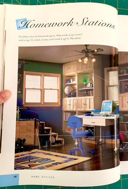 An open book or magazine page showing a color photograph of a home office interior with a desk, chair, shelves, and computer, captioned 'Homework Stations' with text above. A hand is holding the left edge of the page.
[additional_image_link]