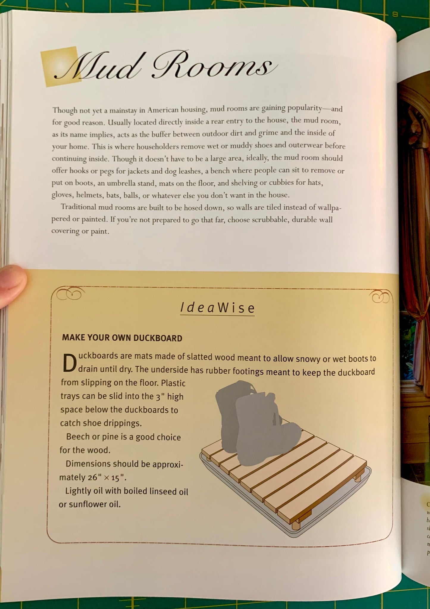 An open book showing printed pages about mud rooms, with a hand holding the left edge. The pages contain text and a small illustration of a wooden duckboard.
[additional_image_link]