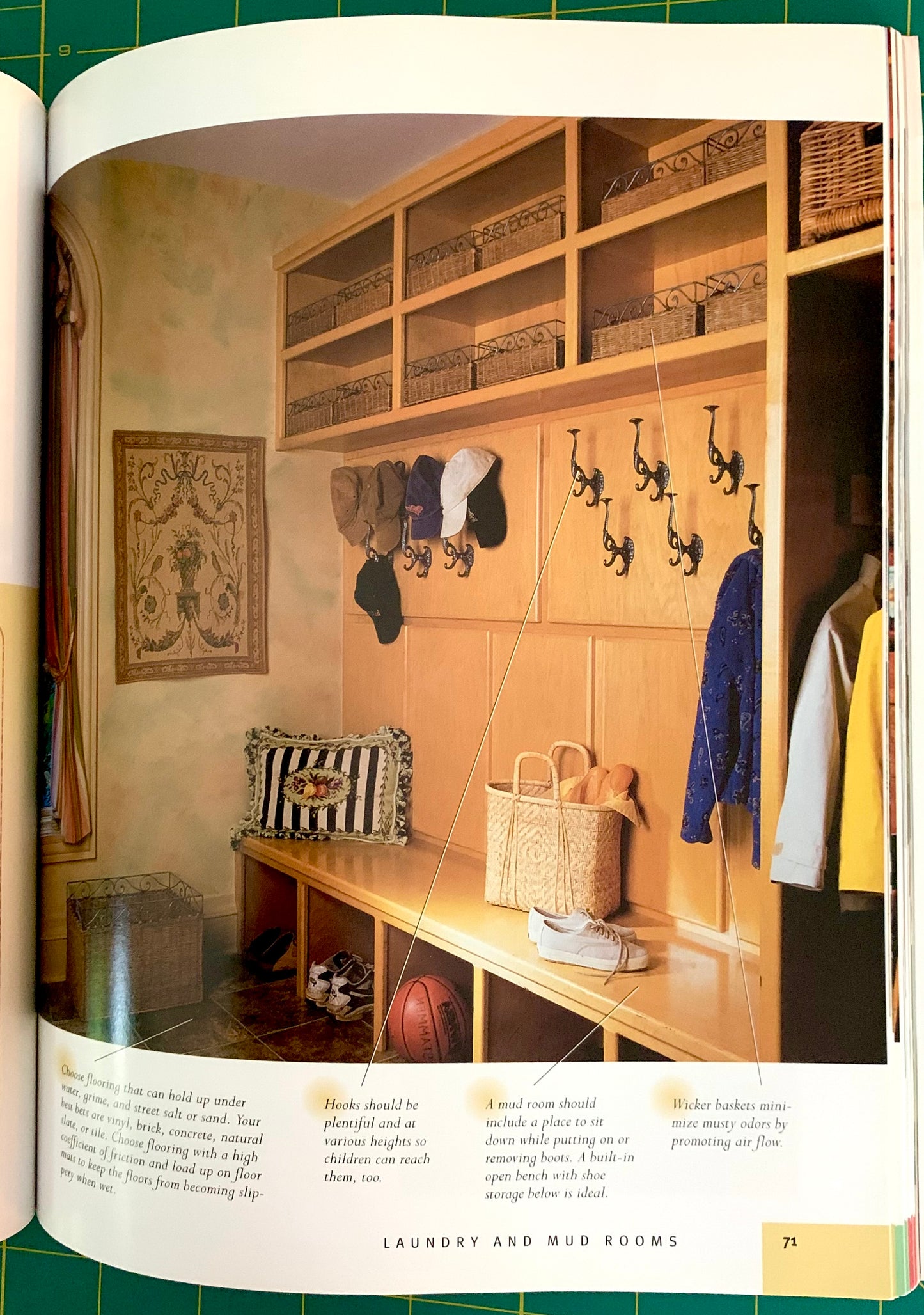 An open book or magazine spread showing a interior photo of a wooden laundry and mud room with shelves, hooks, baskets, and hanging clothes. The page includes text blocks and a small color swatch near the bottom.
[additional_image_link]