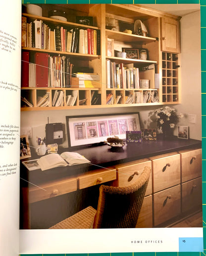 An interior room scene showing a home office setup with light wood built-in shelving, a dark desk, a wicker chair, books, framed wall art, and small decor items. This appears to be a magazine or catalog interior page rather than a clean isolated product shot.
[additional_image_link]