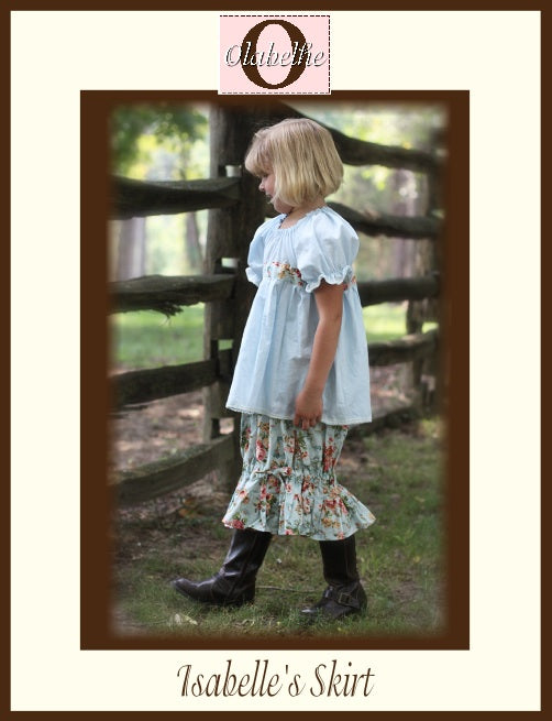 A child wearing a light blue short-sleeve top and a floral tiered skirt with dark boots, standing outdoors beside a wooden fence. The image includes a decorative border and text reading 'Isabelle's Skirt' and 'Olabelhe'.
Photo by Olabelhe [image_link]
