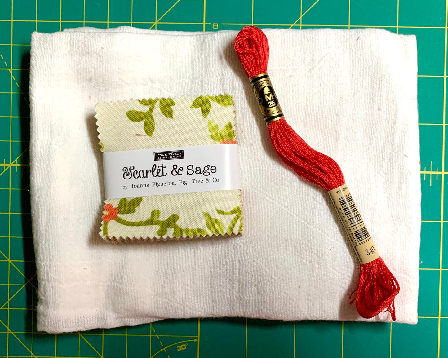 Red embroidery floss and fabric swatch on a white fabric background with a green cutting mat.
Photo by Karen King [additional_image_link]
