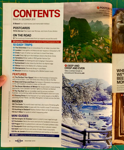 An open magazine or booklet spread showing the 'CONTENTS' page with text, a mountain landscape photo, and a travel guide cover, photographed on a green surface.
[additional_image_link]