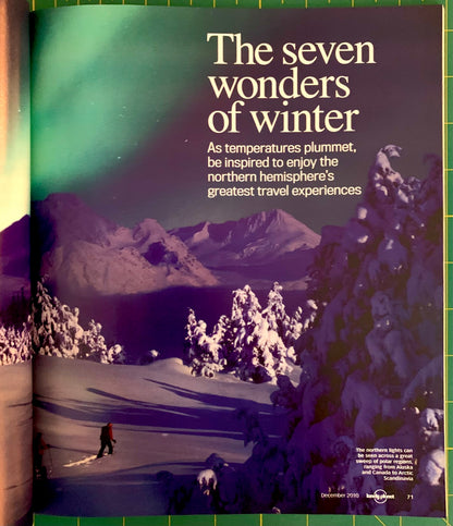 A printed travel poster or magazine spread titled "The seven wonders of winter" showing snowy mountains, frozen trees, and a skier under a green aurora sky. The text references northern hemisphere travel experiences, and a small Lonely Planet logo appears at the bottom.
[additional_image_link]