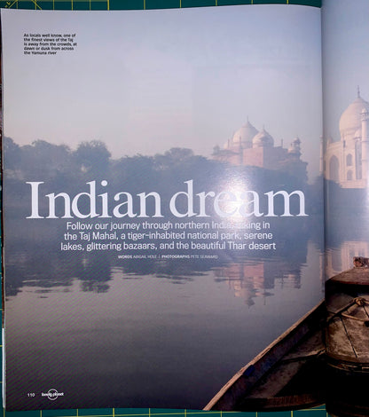 An open magazine or book spread showing a travel article titled 'Indian dream' over a scenic photograph of the Taj Mahal reflected in water, with a boat in the foreground and a green cutting mat visible around the edges.
[additional_image_link]
