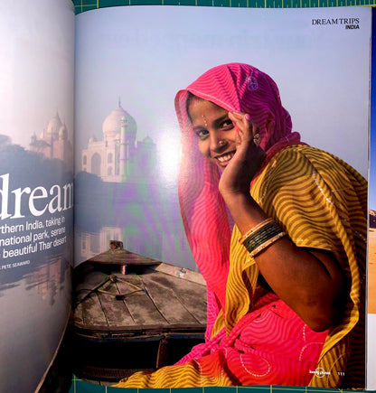 A printed travel magazine or book spread featuring a portrait of a smiling woman in a bright pink and yellow sari with a Taj Mahal background, alongside the text 'DREAMTRIPS INDIA' and 'PTE SHANMUG'.
[additional_image_link]